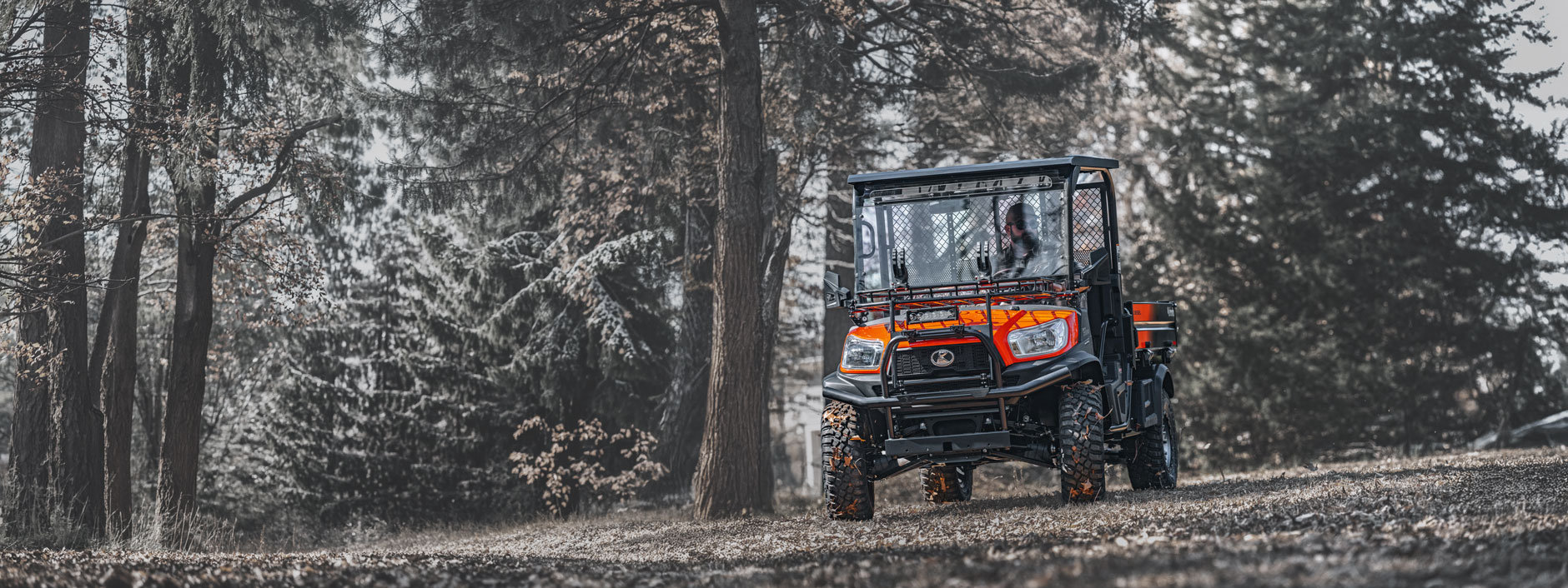 Kubota zero-turn mower and RTV utility vehicle parked on a lawn in front of a barn